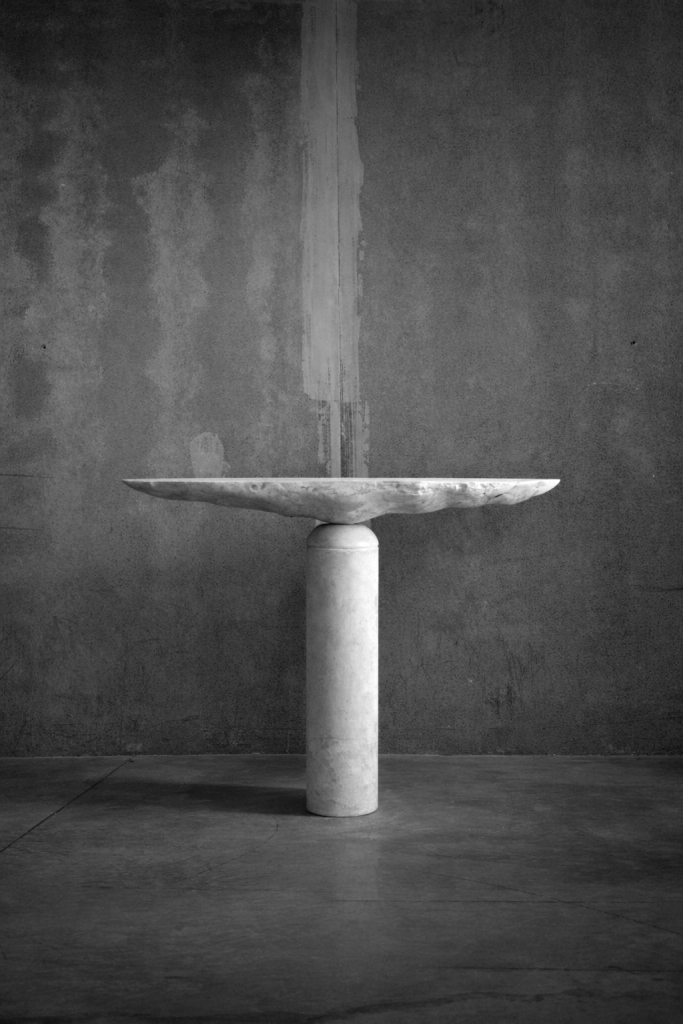 Profile view of monolithic stone pedestal table by sculptor Isac Elam Kaid showing continuous stone surface and cylindrical base.