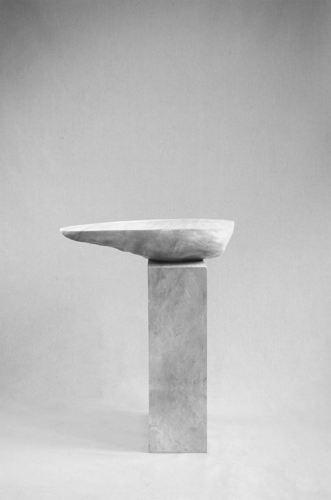 Asymmetrical stone side table by Isac Elam Kaid with an irregular eroded stone top balanced on a rectilinear stone plinth.