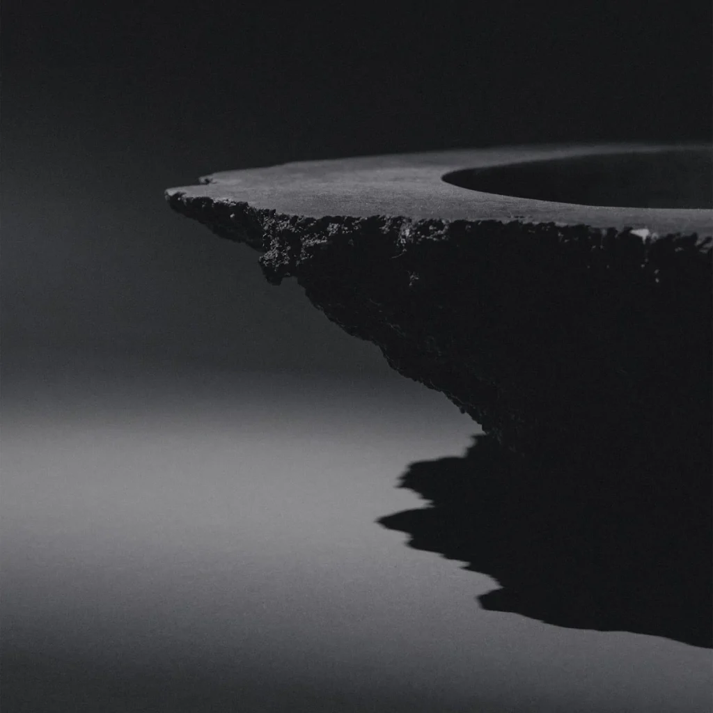 Sculptural blackened bronze vessel K25-2203 by Isac Elam Kaid with fractured edge and smooth interior basin.