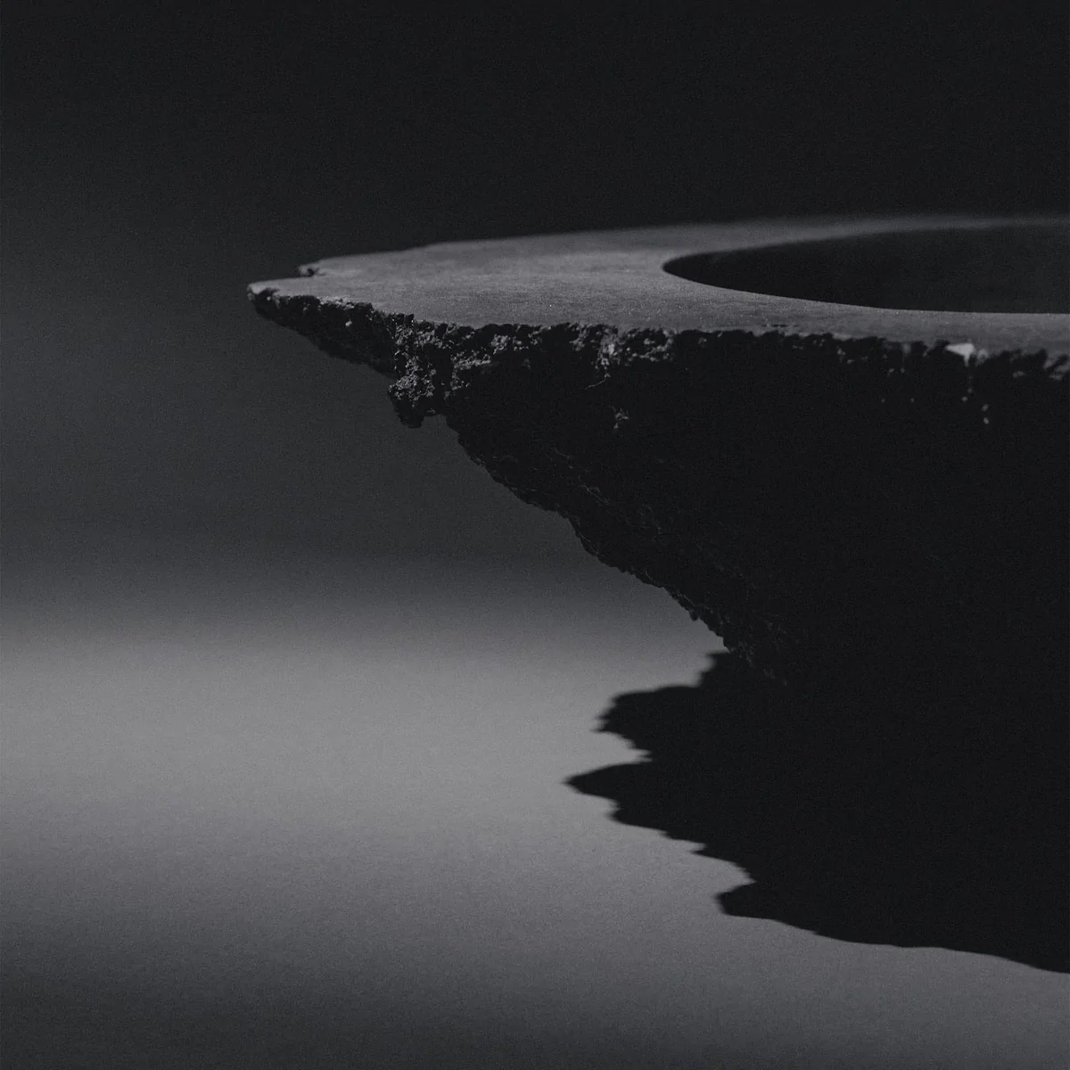 Sculptural blackened bronze vessel K25-2203 by Isac Elam Kaid with fractured edge and smooth interior basin.